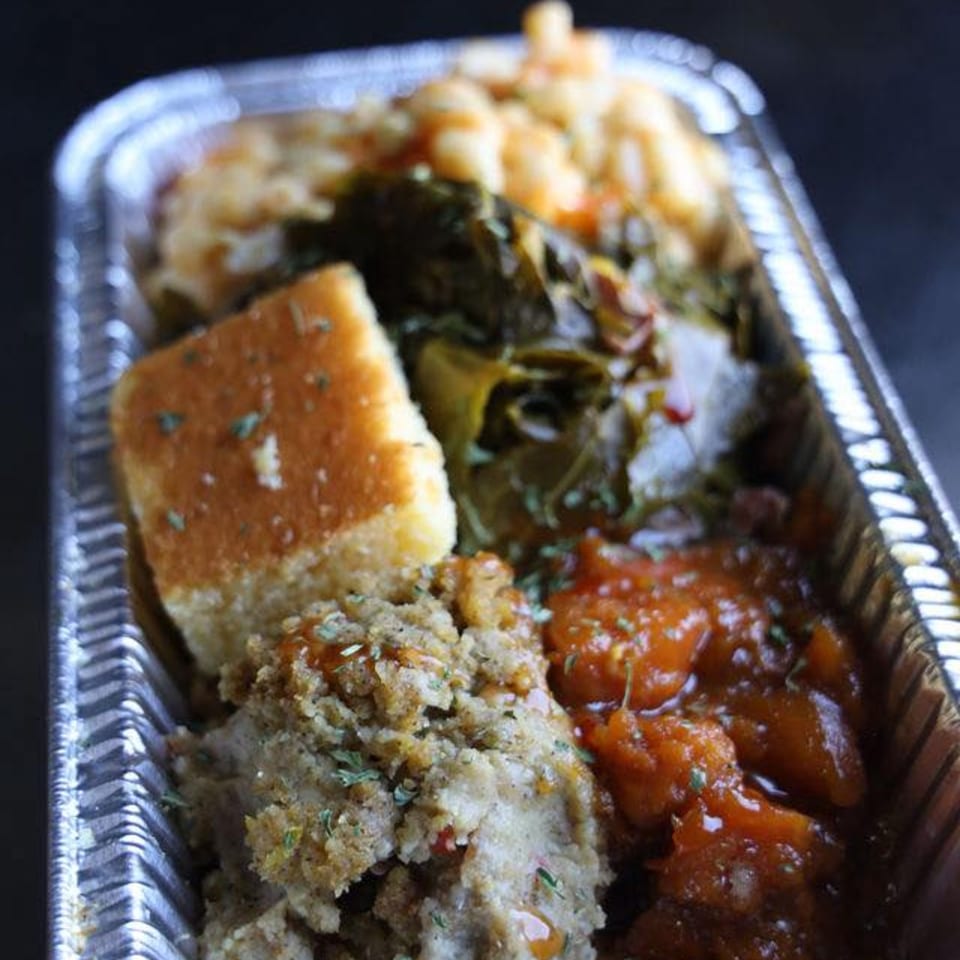 A Jive Turkey soul food meal in a foil container with cornbread, stuffing, collard greens, and mac and cheese.